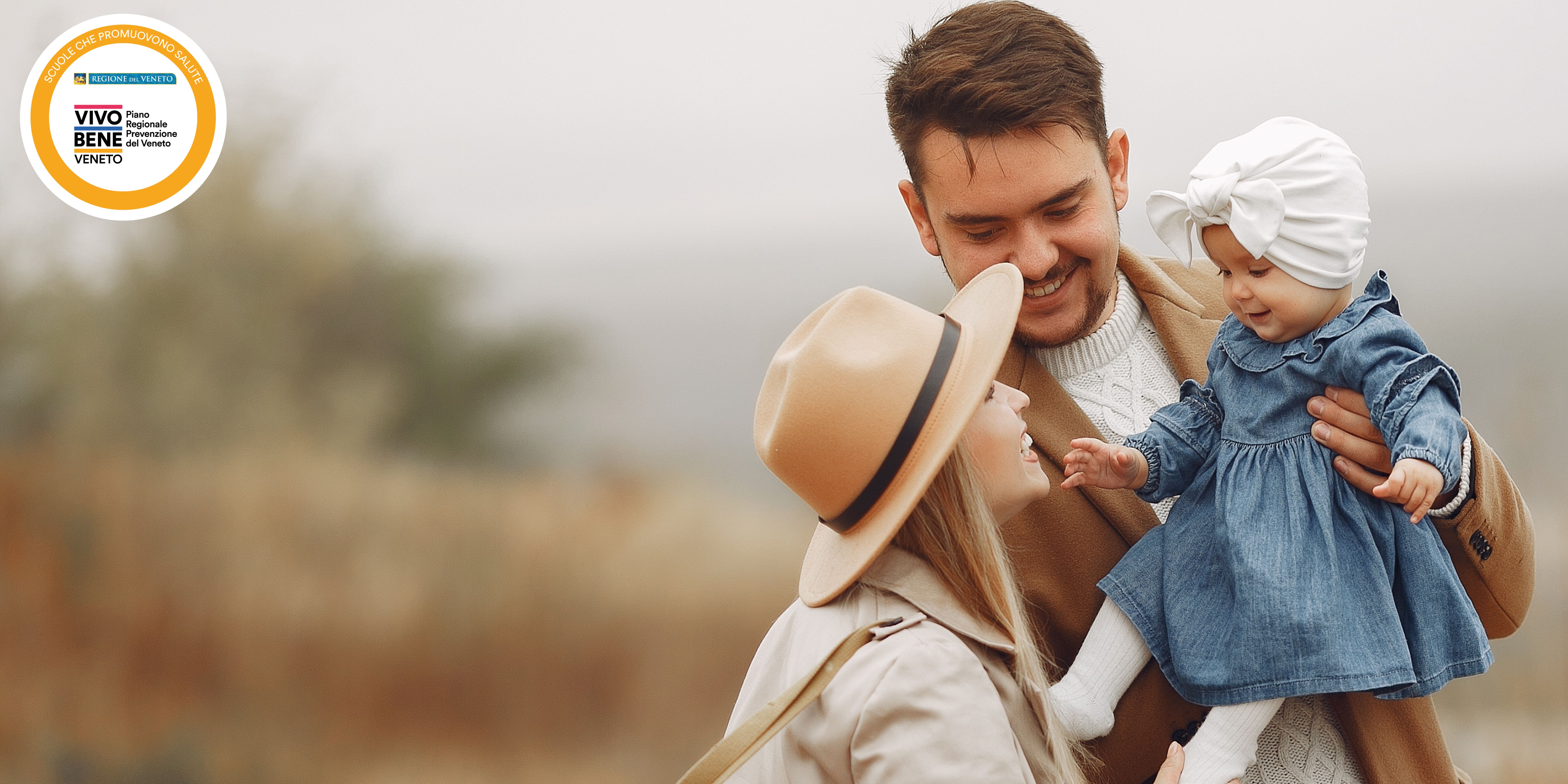 Immagine di una coppia di genitori felici che tengono in braccio una bambina di pochi mesi. Nell'angolo in alto a sinistra, il logo della rete delle Scuole che Promuovono Salute del Veneto