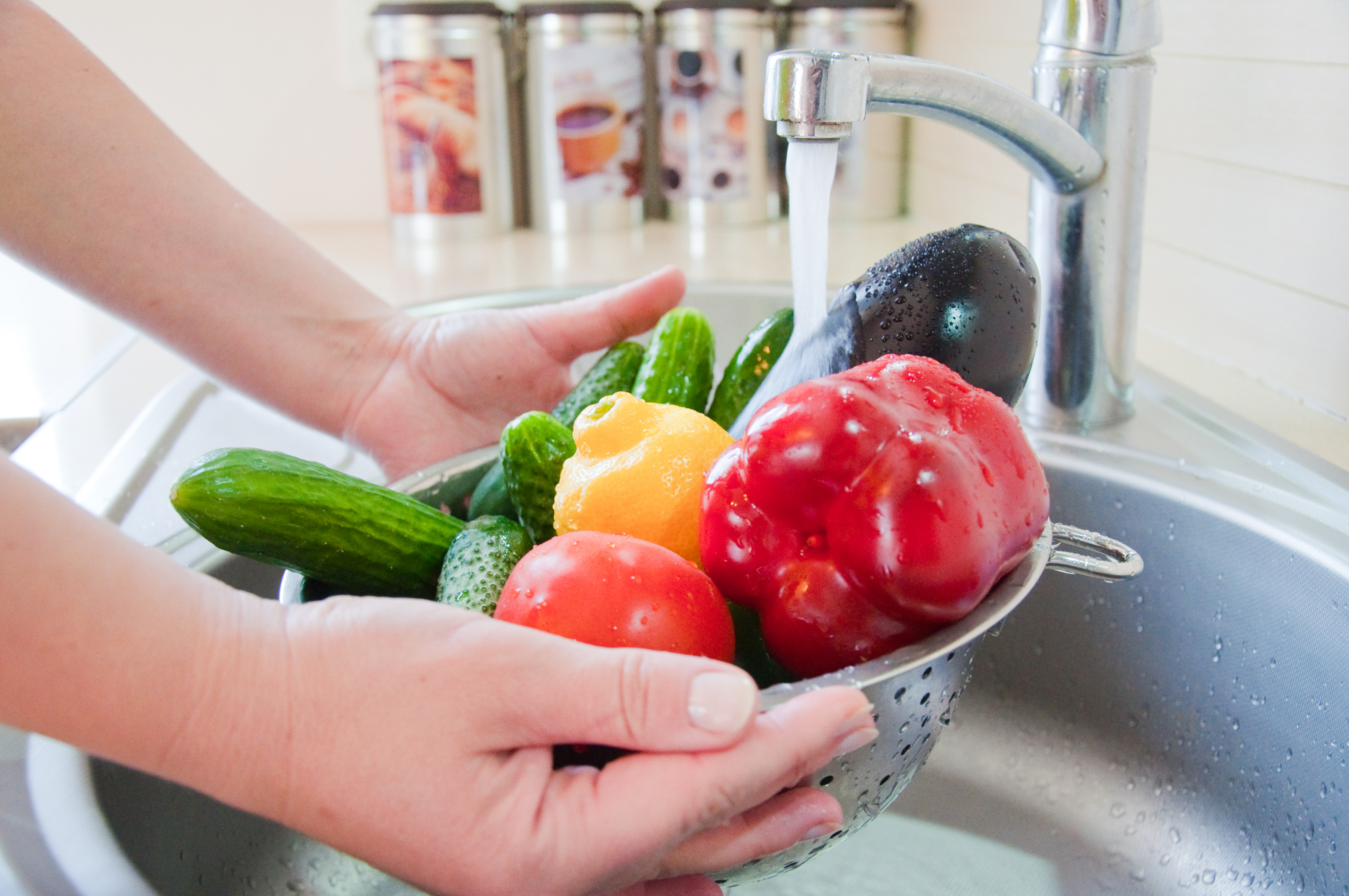 Immagine di mani che tengono uno scolapasta pieno di verdure sotto l'acqua corrente del lavello